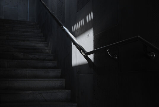 Sunlight Pattern Cast on Wall of Dark Staircase with Handrail