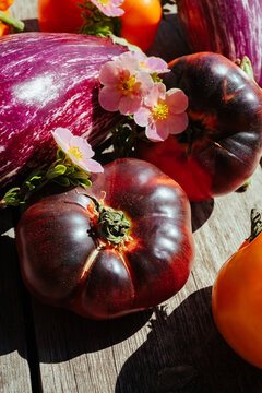 Fresh vegetables and flowers on wooden surface in sunlight