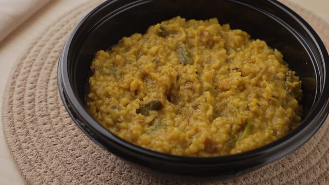 Freshly Cooked Yellow Moong Dal Khichdi with Turmeric Served Hot in a Black Bowl, Close-Up Food Shot.