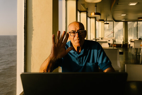 Elderly man waving during a video call in a sunlit living room.
