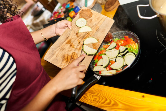 Woman cooking fresh vegetables in a pan on stove