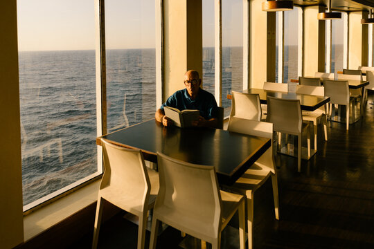 Wide shot of an elderly man sitting alone in a living room, reading