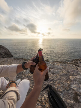 Couple toasting with beer on cliff overlooking sea at sunset