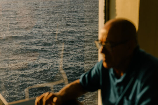 Elderly man relaxing by a ship porthole overlooking the ocean sunset.