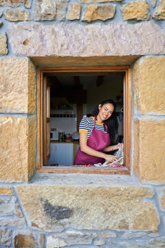 Smiling woman unpacking fresh produce in rustic kitchen window