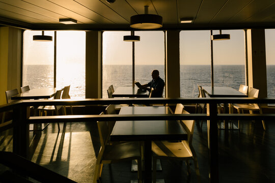 Silhouette of an elderly man holding a book by a boat window at sunset