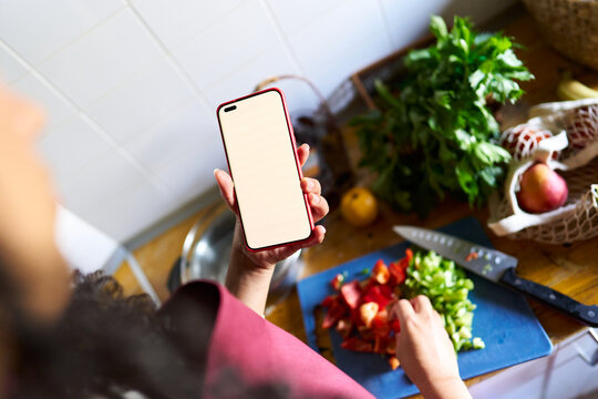 Woman holding smartphone with blank screen cooking healthy food