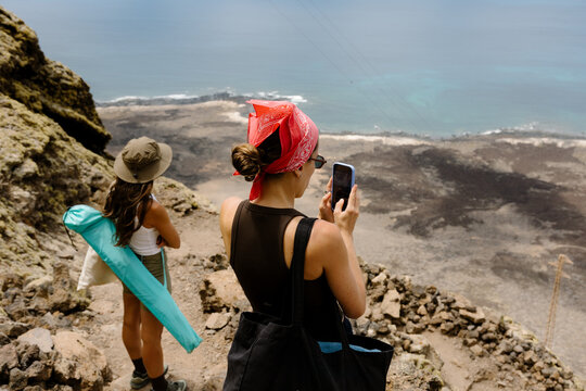 Woman taking smartphone photos of Lanzarote views from a cliff.