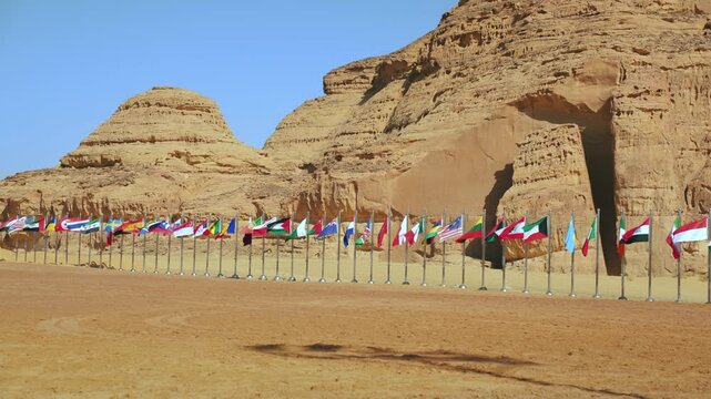 Row of different world countries flags waving in slow wind near large rocky cliff on a sunny day