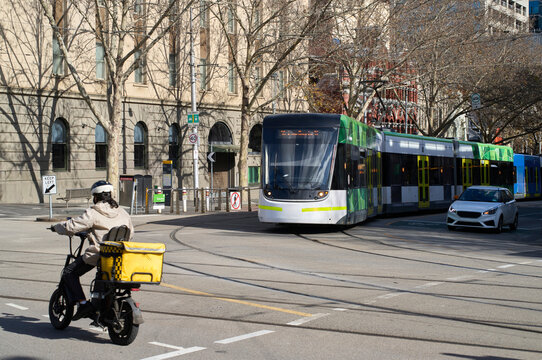 Food Delivery Rider Navigates City Streets With Tram in Background