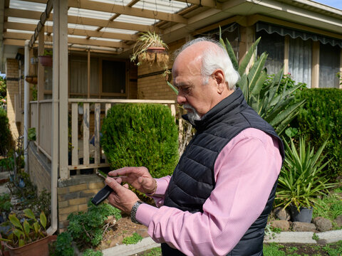 Elderly Man Checks His Phone Outside His Home During Daytime