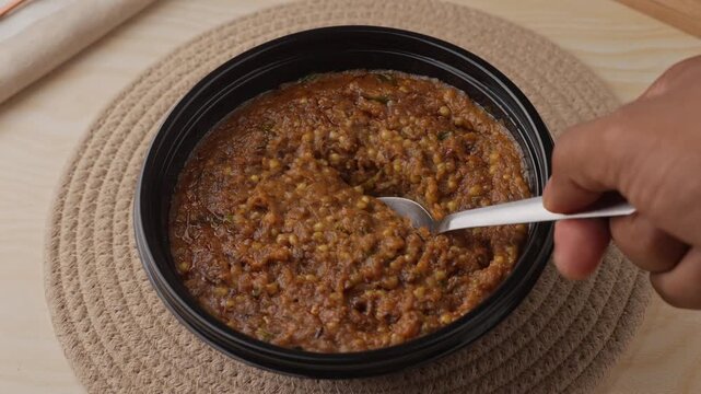 Freshly Cooked Healthy Millet Khichdi Served Hot in a Black Bowl, Close-Up Food Shot of being picked with a spoon.