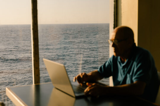Out of focus elderly man working remotely using his laptop