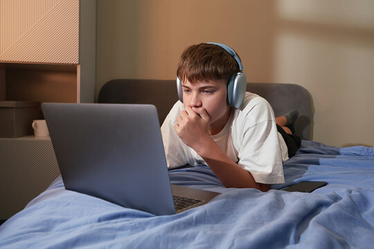 Teen boy online learning watching laptop on bed with headphones
