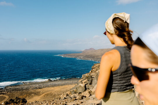Two women in athletic wear admiring a volcanic coastline.