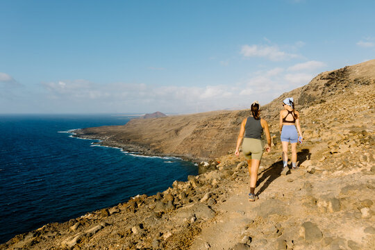 Two female hikers walking along a coastal cliff trail in Lanzarote.