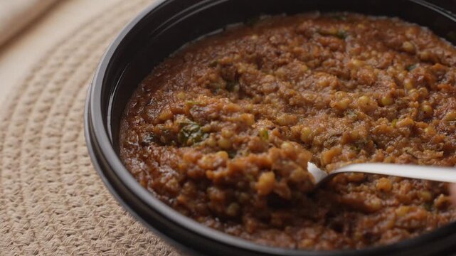 Freshly Cooked Healthy Millet Khichdi Served Hot in a Black Bowl, Close-Up Food Shot of being picked with a spoon.