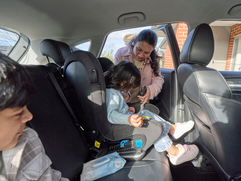 Mother Helps Child Buckle Seatbelt in Baby Seat in Rear of Car