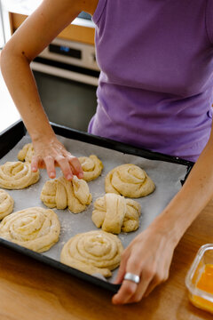 Woman arranging raw cinnamon sticks on parchment paper at home.
