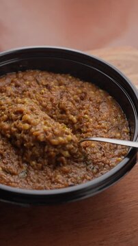 Freshly Cooked Healthy Millet Khichdi Served Hot in a Black Bowl, Close-Up Food Shot of being picked with a spoon.