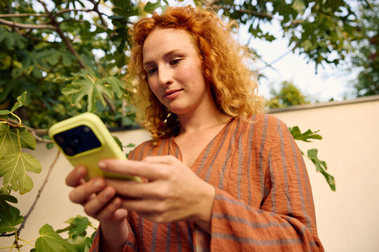 Ginger woman uses her phone in the backyard
