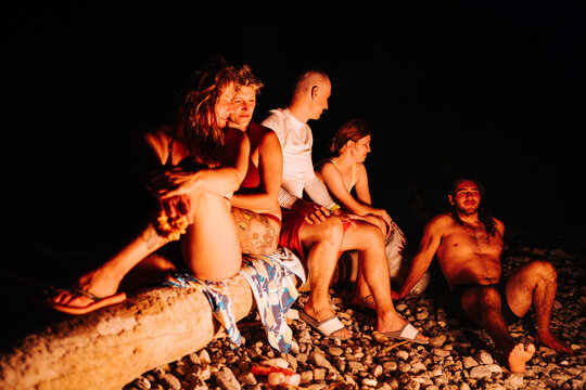 friends sitting on driftwood beside a beach campfire