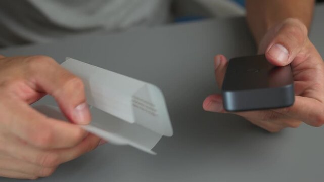 Close-up hands peeling backing from adhesive bandage strip from compact dispenser readying application to fingertip under soft studio light and neutral tabletop background