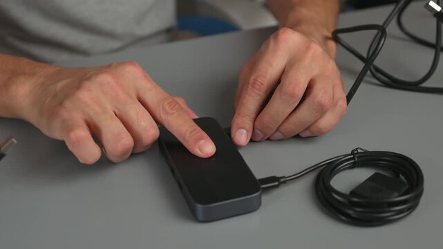 Hands connecting and testing wired computer mouse on desk with USB cable and button presses visible in close-up view for hardware setup and workspace action scene.