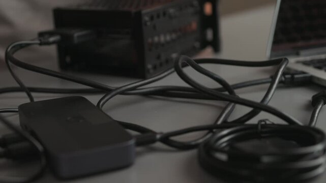 Hands connecting external hard drive enclosure to laptop with USB cable on tabletop, closeup of portable storage setup and hardware connection view from slight overhead angle, neutral soft lighting, t
