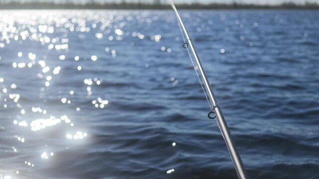 POV shot from an inflatable boat showing a fishing rod with slow glistening waves and a northern shore with dwarf vegetation.