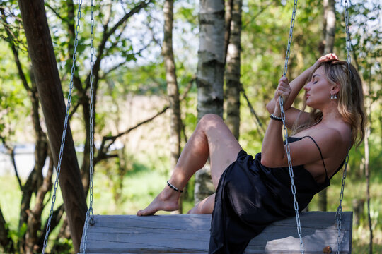 Elegant Blonde Woman Posing on a Wooden Swing in a Summer Garden