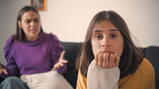 Young Hispanic woman looking at the camera while her friend argues with her in the background. Concept of conflict, friendship tension, and interpersonal relationships.