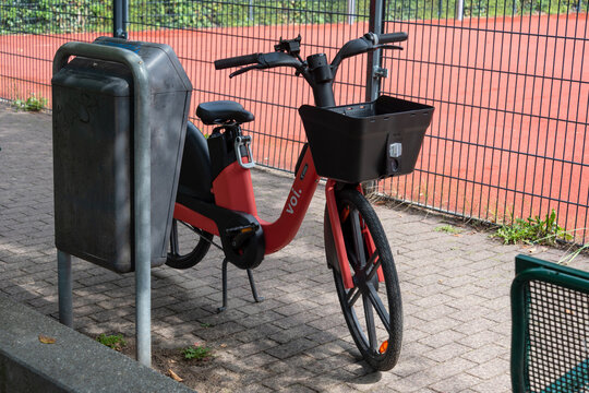 Berlin, Germany - 16 August 2026. Orange electric rental bike parked on a city sidewalk next to a grassy verge. Urban bike sharing, electric mobility, sustainable transport, city lifestyle.