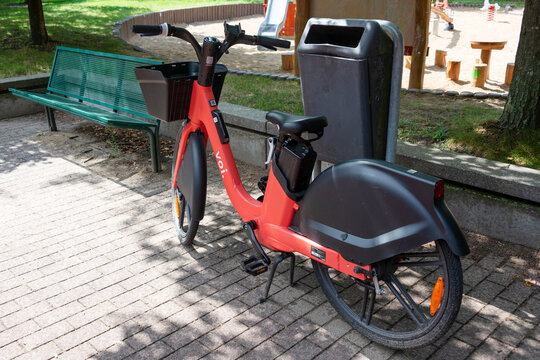 Berlin, Germany - 16 August 2026. Red shared electric bike parked beside a bench near a playground in a city park. Urban mobility, shared transport, sustainability, family leisure, outdoor recreation.