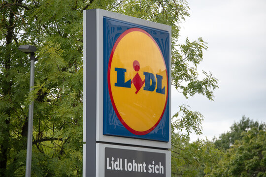 Berlin, Germany - 16 August 2026. Lidl storefront sign stands beside a tree-lined road at the supermarket entrance. Retail, shopping, brand signage, urban streetscape, convenience, consumer culture.
