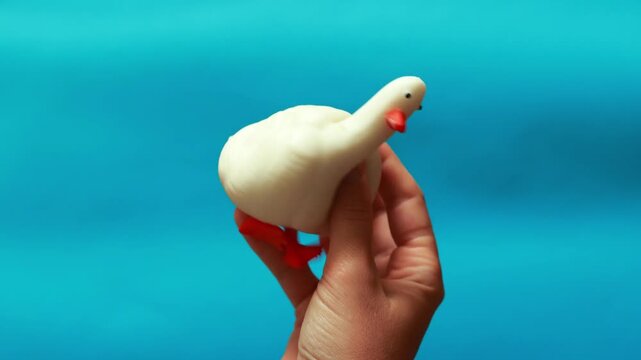 Hand squeezing a white duck anti-stress squishy toy on a blue background. Stress relief, fidget toy, sensory play, and mental health relaxation concept