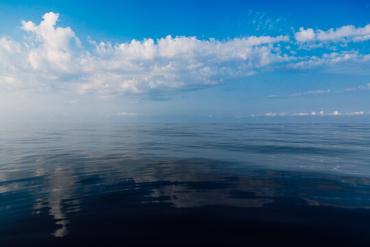 Wide blue sea beneath a dramatic cloud-filled sky, with reflections creating a peaceful scenic travel background.