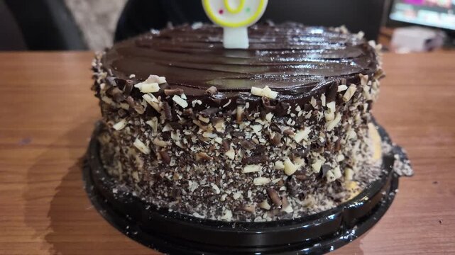 Dark chocolate cake with chopped nuts. Celebratory number eight candle. Tabletop setting with warm lighting. Background shows blurred office environment. Emotions: cheerful, festive, joyful