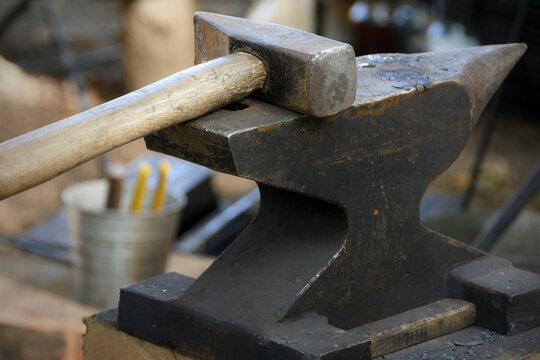 The photo shows a blacksmith's anvil (single-horned, English style) and a blacksmith's hammer with a wooden handle resting on it.