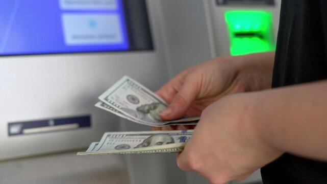 Man counting US dollar cash beside an ATM. Hands hold a stack of banknotes near a cash machine. Money withdrawal, banking service, transaction, savings, budget and personal finance concept