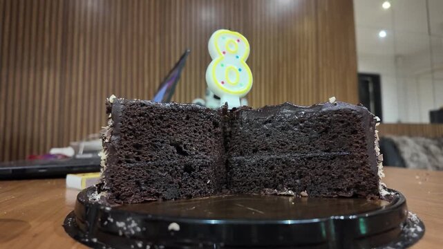 Hand cuts slice from chocolate cake. Candle shaped like number eight glows. Mini pumpkin sits beside cake slice. Joyful gesture shows celebration moment. Ideal for birthday or Halloween themes