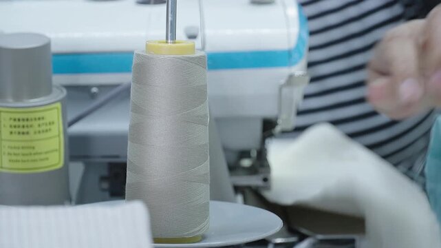 Overlock machine with thread cone, worker sewing fabric at a textile factory