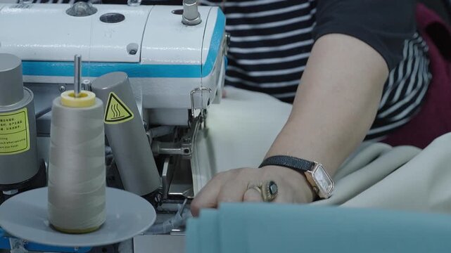 Seamstress working on an overlock sewing machine with thread cone at a garment factory