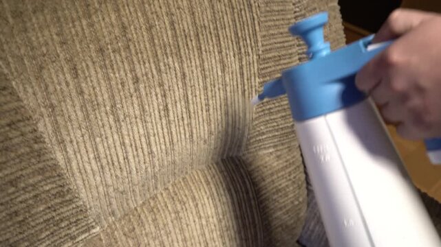 Close-up of professional upholstery cleaning in action, with cleaning solution being sprayed onto a sofa fabric to remove dirt, stains, and grime. 