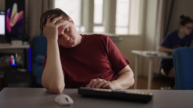 Exhausted male student, freelancer sitting at desk, feeling stressed and overworked, freelancer man looking at camera with tired expression, showing signs of burnout and procrastination, slow motion.