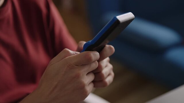 Close-up cropped shot of person hands holding playing old school handheld video game, pressing yellow buttons of blue device for leisure and nostalgic entertainment at home. Shooting in slow motion.