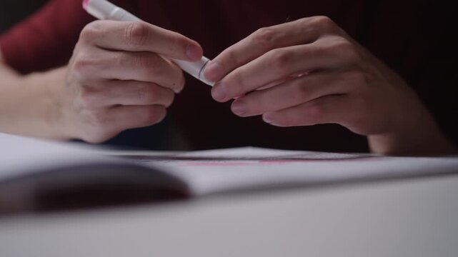 Close-up of person uncapping pink felt tip pen and drawing line on paper. Focus on hands and creative process of writing, studying, sketching in notebook, closeup, cropped shot, slow motion.