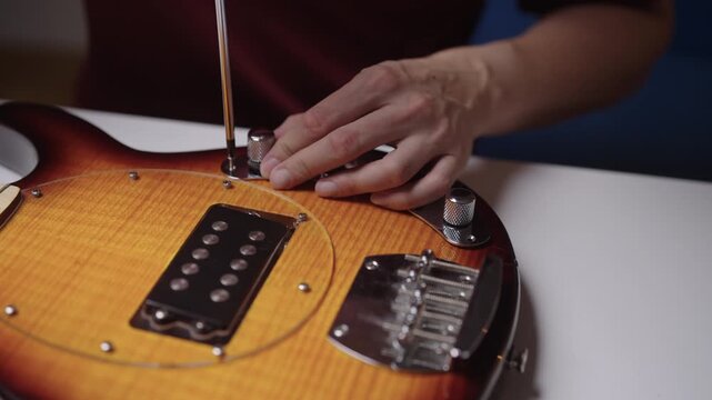 Closeup of skilled luthier hands assembling unique handcrafted electric guitar, using screwdriver to tighten metal volume and tone control knobs on wooden body, close-up, cropped shot, slow motion.