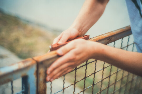 Close-up of hands using a sanding block to smooth a rusty metal fence before painting. Motion blur adds a raw, authentic feel. DIY restoration photo for craft and renovation projects