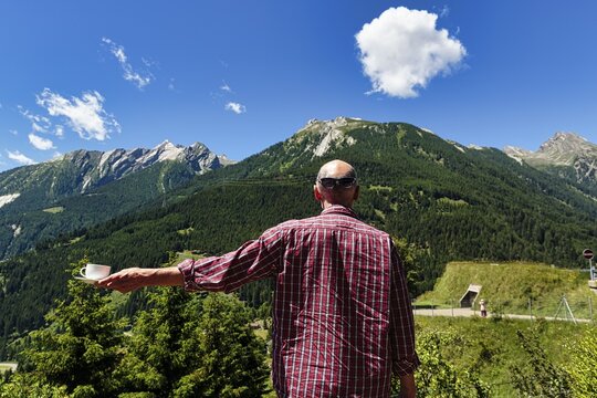 Traveller, Best Ager with rumpled shirt and sunglasses on back of head, holding a coffee cup, enjoying unusual break with beautiful view of the Alps, Switzerland
